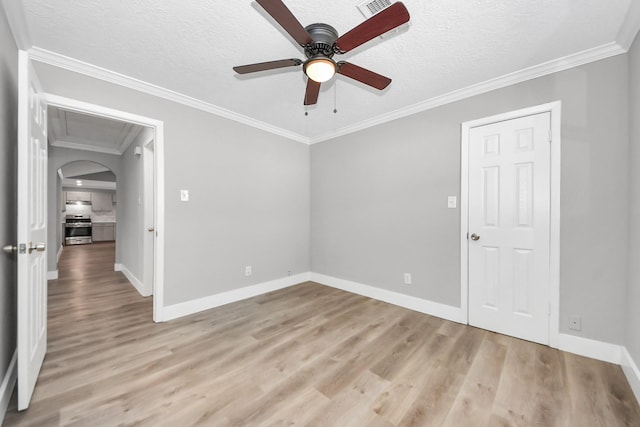 empty room with light wood-type flooring, crown molding, arched walkways, and a textured ceiling