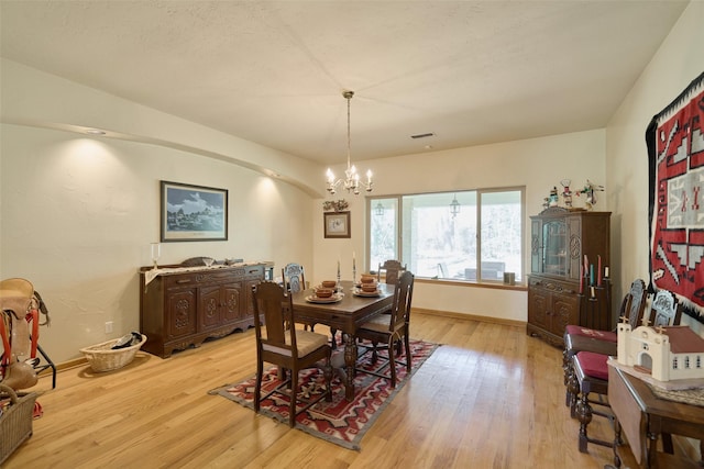 dining space with light wood finished floors, a notable chandelier, visible vents, and baseboards