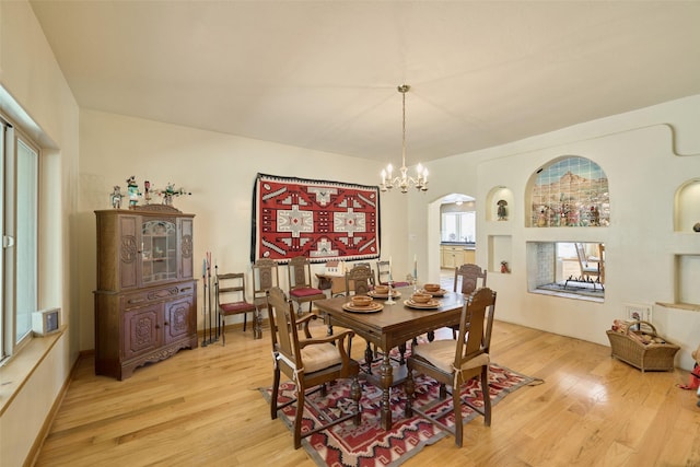 dining space featuring arched walkways, light wood-type flooring, and a chandelier