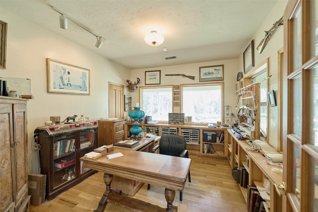 office space with track lighting, light wood-style flooring, a workshop area, and visible vents