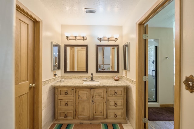 bathroom with visible vents, a textured ceiling, a shower stall, wainscoting, and vanity