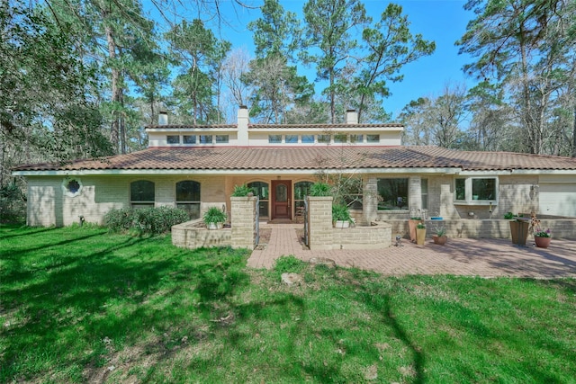 back of property with a lawn, a tile roof, a patio, brick siding, and a chimney