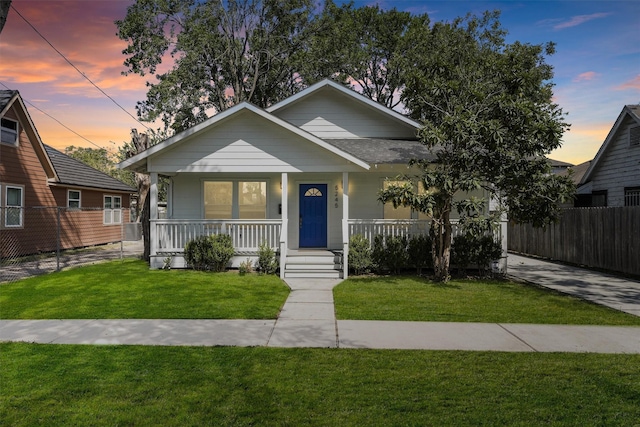 bungalow-style house with covered porch, fence, and a front lawn