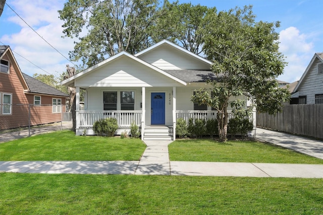 bungalow-style house featuring a porch, roof with shingles, fence, and a front lawn