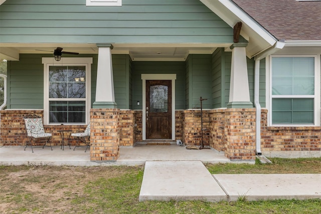 entrance to property with ceiling fan, brick siding, roof with shingles, and a porch