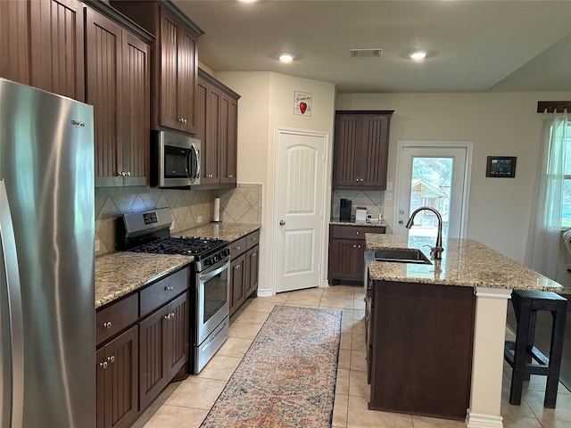 kitchen featuring light stone counters, a center island with sink, visible vents, appliances with stainless steel finishes, and a sink