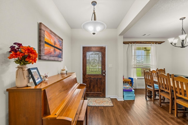 foyer entrance with baseboards, dark wood finished floors, visible vents, and an inviting chandelier