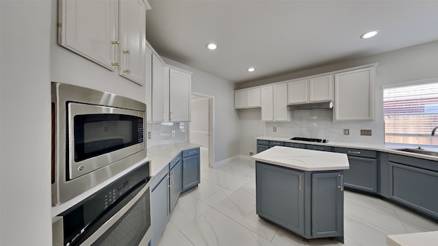 kitchen with marble finish floor, stainless steel appliances, backsplash, gray cabinetry, and under cabinet range hood