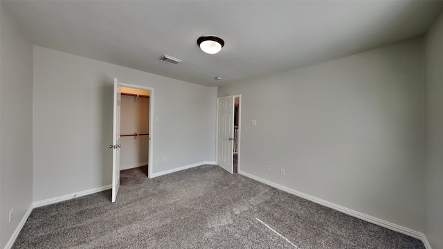 unfurnished bedroom with a closet, visible vents, dark carpet, a spacious closet, and baseboards