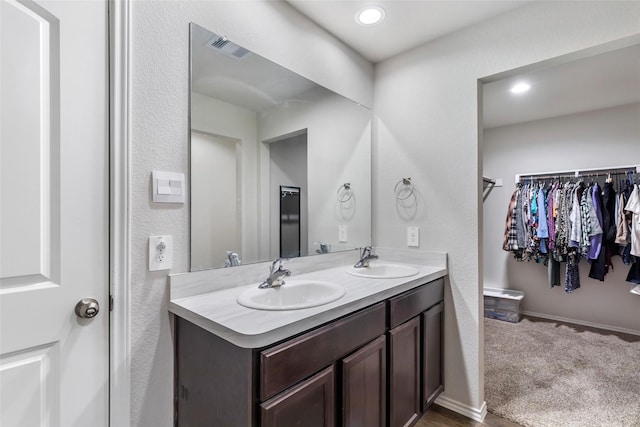 full bathroom featuring double vanity, a sink, visible vents, and a walk in closet