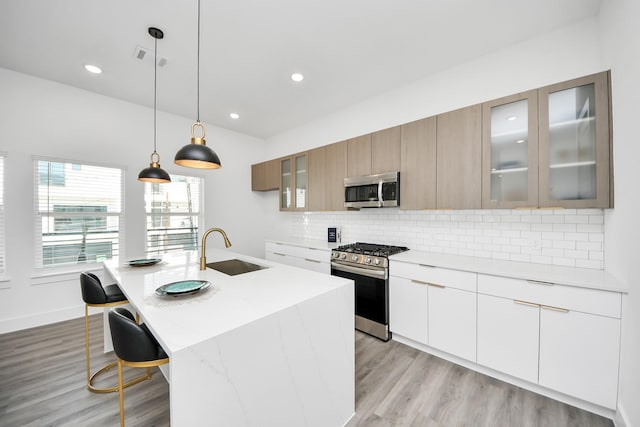 kitchen with stainless steel appliances, a sink, light countertops, backsplash, and an island with sink