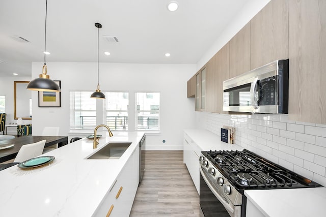 kitchen with modern cabinets, appliances with stainless steel finishes, light stone counters, a sink, and backsplash