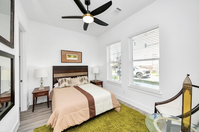 bedroom with ceiling fan, wood finished floors, visible vents, and baseboards