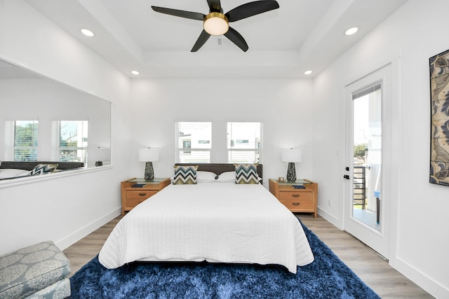 bedroom with baseboards, a tray ceiling, light wood-type flooring, and access to exterior