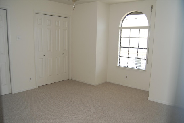 unfurnished bedroom featuring light carpet, baseboards, and a closet