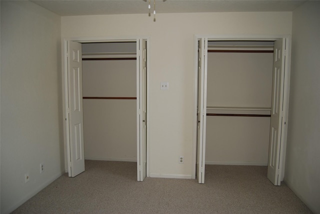 unfurnished bedroom with light colored carpet, baseboards, and two closets