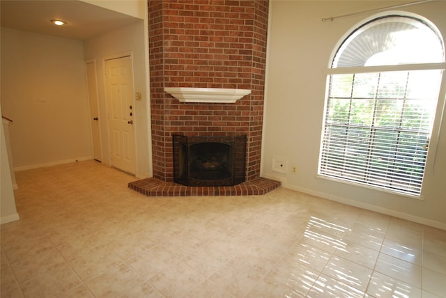 unfurnished living room featuring a brick fireplace and baseboards