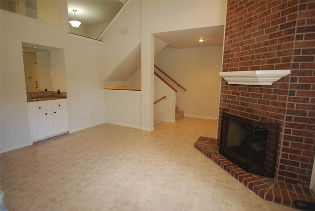 unfurnished living room featuring a brick fireplace, stairway, and baseboards