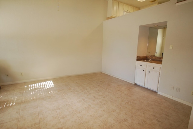 unfurnished room with light tile patterned floors, a high ceiling, a sink, and baseboards