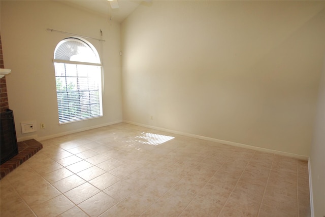 unfurnished room featuring a ceiling fan, a brick fireplace, baseboards, and light tile patterned floors