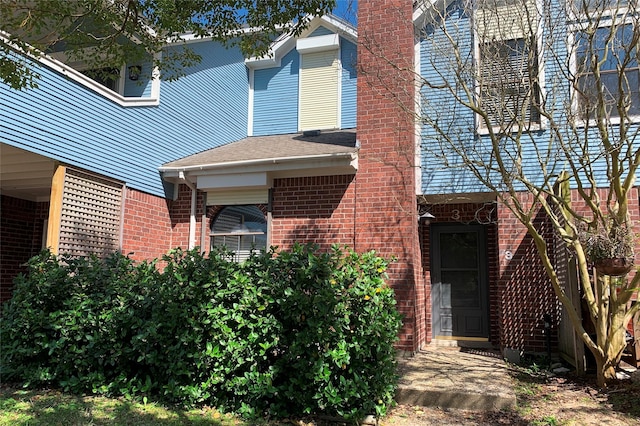 exterior space featuring roof with shingles and brick siding