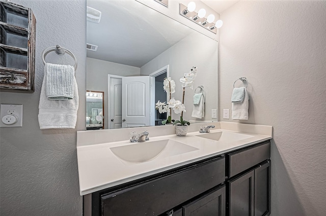 full bath with a textured wall, double vanity, a sink, and visible vents