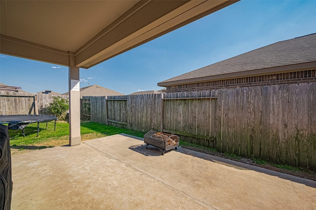 view of patio with an outdoor fire pit, a trampoline, and a fenced backyard