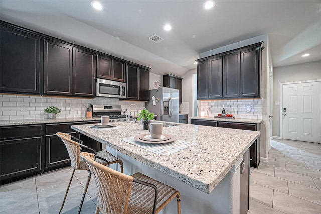 kitchen featuring light tile patterned floors, a breakfast bar area, visible vents, appliances with stainless steel finishes, and light stone countertops