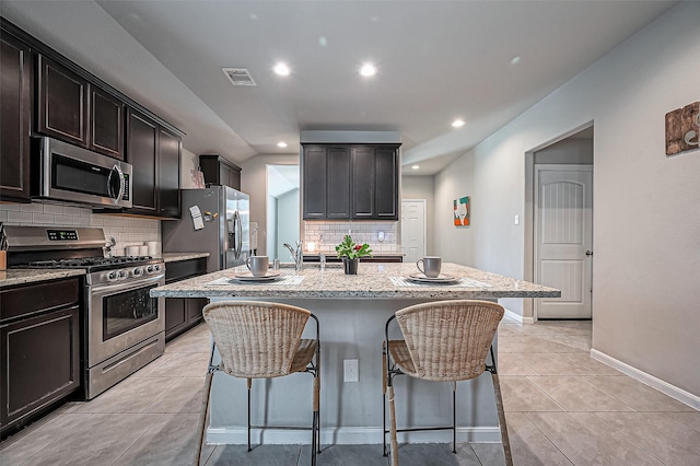 kitchen with light tile patterned floors, a breakfast bar area, appliances with stainless steel finishes, light stone counters, and a sink