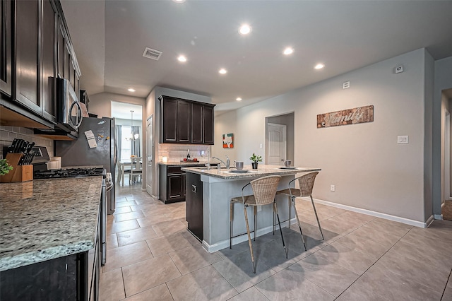 kitchen with light tile patterned floors, a center island with sink, visible vents, stainless steel appliances, and a kitchen bar