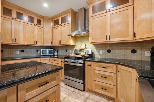 kitchen featuring tasteful backsplash, appliances with stainless steel finishes, light tile patterned flooring, dark stone counters, and wall chimney exhaust hood