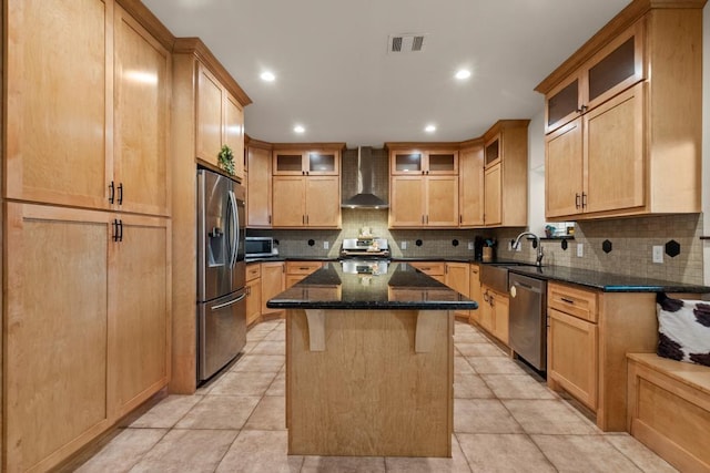 kitchen with visible vents, appliances with stainless steel finishes, a kitchen island, wall chimney range hood, and a sink