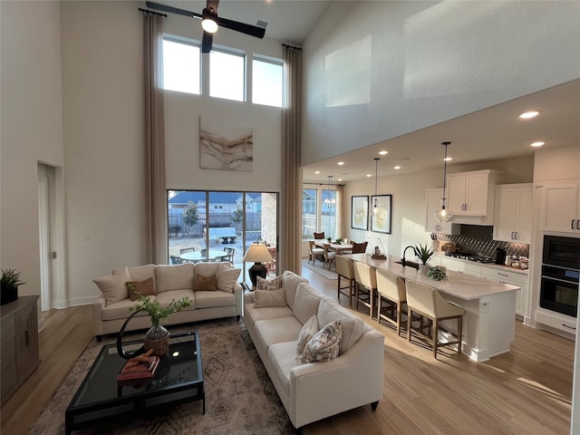 living area with a high ceiling, recessed lighting, a ceiling fan, and light wood-style floors