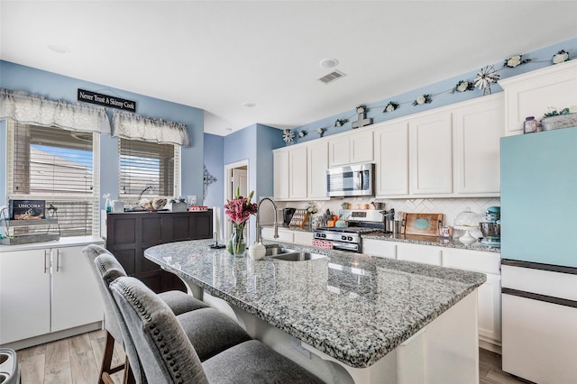 kitchen with a kitchen island with sink, stainless steel appliances, a sink, visible vents, and light wood finished floors