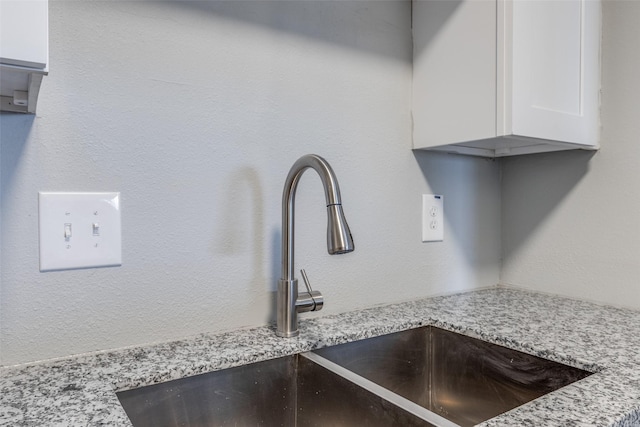 details with light stone counters, a sink, and white cabinetry