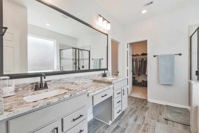 bathroom with a walk in closet, visible vents, a sink, and a shower stall