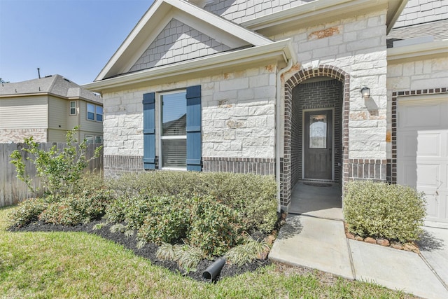 entrance to property featuring an attached garage, stone siding, and fence