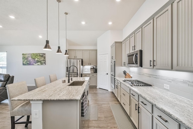 kitchen featuring a breakfast bar area, stainless steel appliances, a sink, light wood-type flooring, and tasteful backsplash