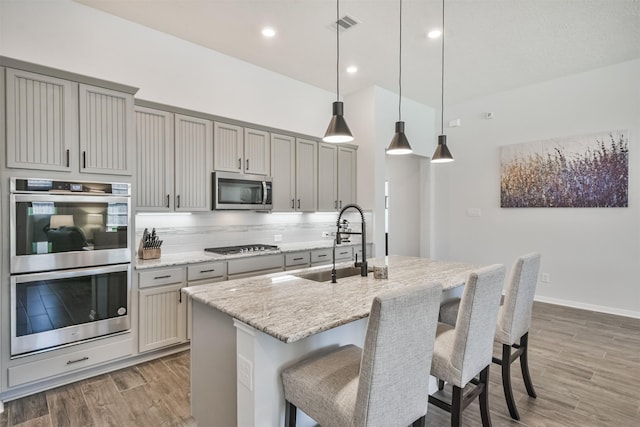 kitchen featuring light wood finished floors, decorative backsplash, appliances with stainless steel finishes, gray cabinetry, and a sink