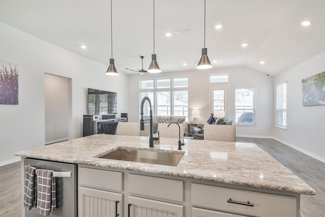 kitchen with light wood-style floors, open floor plan, a sink, light stone countertops, and dishwasher