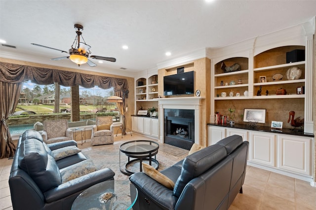 living room featuring ceiling fan, built in shelves, a fireplace, visible vents, and ornamental molding