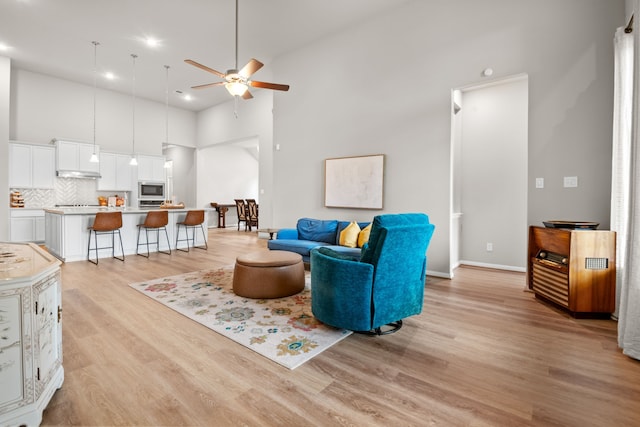 living area with ceiling fan, baseboards, a towering ceiling, and light wood-style floors