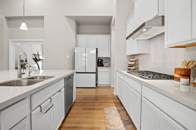 kitchen with appliances with stainless steel finishes, extractor fan, light wood-style floors, white cabinetry, and a sink