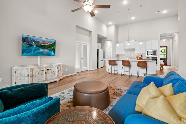 living area with light wood finished floors, a high ceiling, visible vents, and a ceiling fan