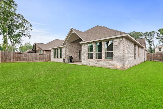 rear view of house with a yard, a fenced backyard, a shingled roof, and brick siding