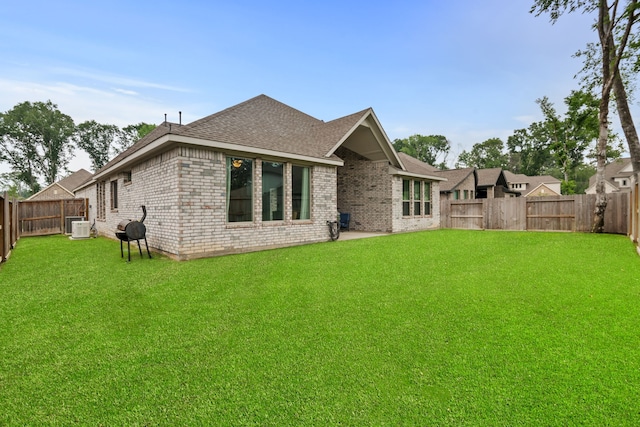 rear view of property with a shingled roof, brick siding, a yard, and a fenced backyard