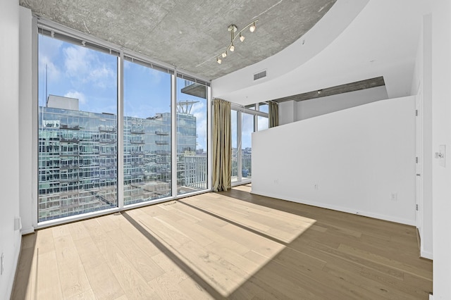 empty room with baseboards, visible vents, wood finished floors, expansive windows, and a city view