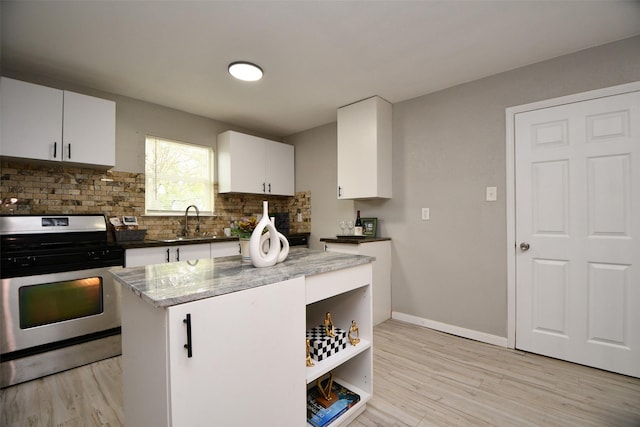 kitchen with stainless steel gas stove, backsplash, light wood-type flooring, white cabinetry, and a sink