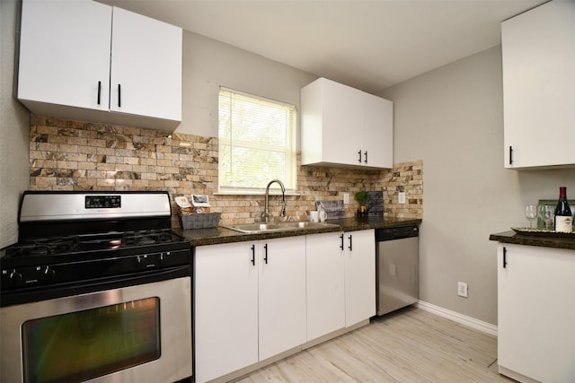 kitchen with tasteful backsplash, dark countertops, appliances with stainless steel finishes, white cabinets, and a sink