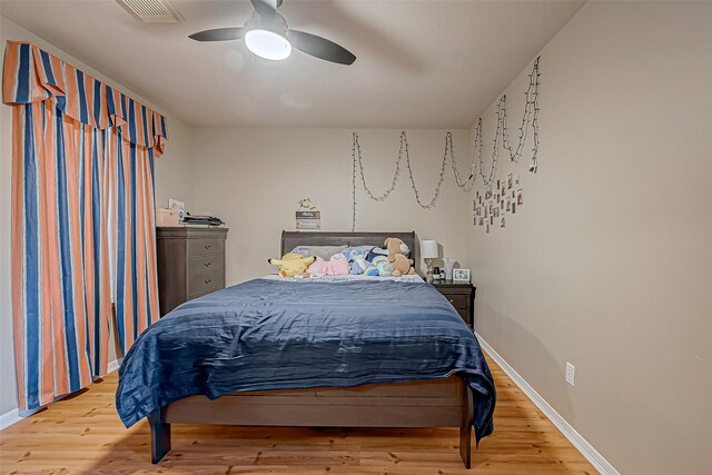 bedroom with ceiling fan, wood finished floors, visible vents, and baseboards